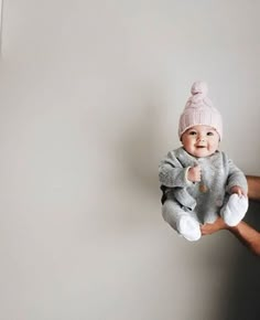 a man holding a baby wearing a pink hat and grey sweater with white trims