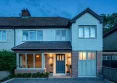 the front of a two story house with blue doors and windows at dusk, lit up by lights on either side of the door