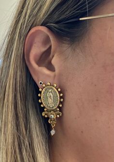 a close up of a person's ear wearing gold and diamond earrings with the image of jesus on it