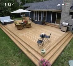 a deck with chairs and an umbrella on the grass near a house in the woods