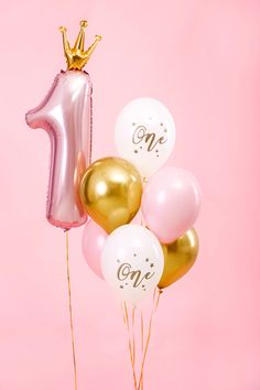 some balloons and a number one balloon on a pink background with a gold foil crown