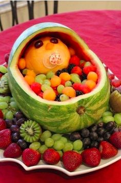 a watermelon boat filled with lots of fruit on top of a red table cloth