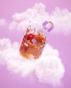 a glass filled with liquid and ice cubes on top of some white fluffy clouds