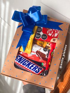 a person holding a box with candy and candies in it that is wrapped in blue ribbon