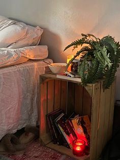 a bed with white sheets and pillows next to a night stand filled with books, candles and plants