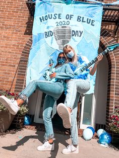 two women are posing in front of a house of blue sign with a guitar on it