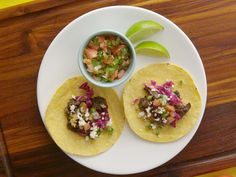 two tacos on a white plate with a small bowl of salsa next to it