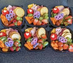 four black plastic containers filled with different types of food and snacks in it's lids