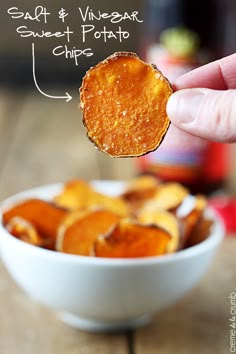 a hand holding up a cracker over a bowl of potato chips with the words salt & vinegar sweet potato chips