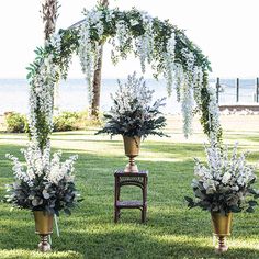 an outdoor ceremony setup with white flowers and greenery in gold vases on the grass