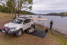 a white car parked next to a lake with a tent on the back and two people standing near it