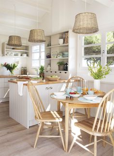 the kitchen table is set for two with plates and bowls on it, along with baskets hanging from the ceiling