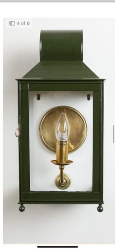 a green and gold wall mounted light with a candle on the front, attached to a white wall