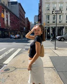 a woman standing on the side of a street next to a cross walk with buildings in the background