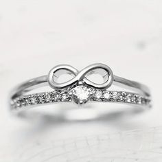 a white gold ring with an infinite love knot and diamond stones in the middle, on top of a marble surface