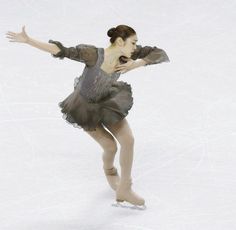 a female figure skating on the ice in a gray and black dress with her arms outstretched