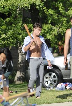 a shirtless man holding a baseball bat while standing in the grass