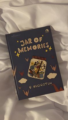 the book is laying on top of the white bed sheet and it says,'jar of memories '