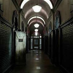 an empty hallway with dark walls and light fixtures on the ceiling, leading to several stalls