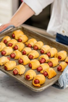 a pan filled with pigs in a blanket on top of a counter next to a person