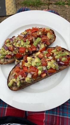 two pieces of bread with avocado and tomatoes on it sitting on a plate