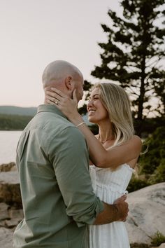 a man and woman standing next to each other in front of the water at sunset