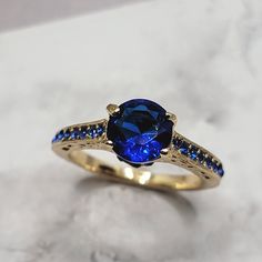 a gold ring with a blue stone surrounded by black and white diamonds on a marble surface