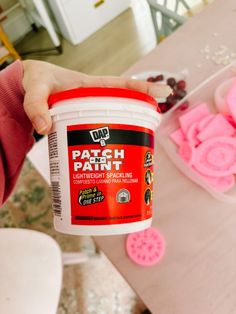 a person holding a container of patch paint on top of a table with other crafting supplies