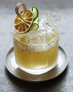 a drink with cucumber and orange slices in it on a silver saucer