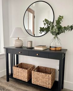 a black console table with two wicker baskets under a round mirror on the wall