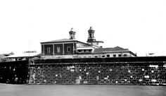 a black and white photo of a brick wall with a clock tower in the background