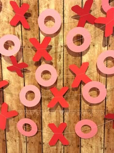 some red and pink paper cutouts are hanging on a wooden wall with string attached to it