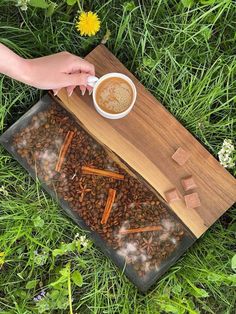 a cup of coffee and some cinnamon sticks on a tray in the grass with flowers