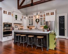 a large kitchen with white cabinets and wooden floors is pictured in this image, there are stools on the island