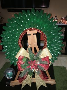 a green wreath with red and gold bows on it sitting on a easel in front of a christmas tree