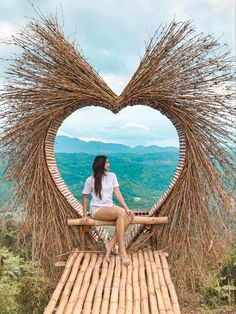 a woman sitting on top of a wooden bench in front of a heart shaped sculpture