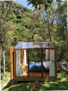 a small house made out of glass and wood in the middle of some grass with trees around it