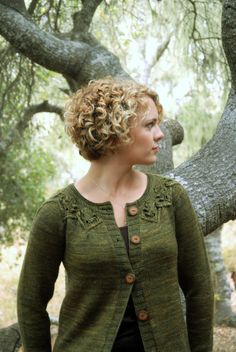 a woman standing in front of a tree wearing a green cardigan and black pants