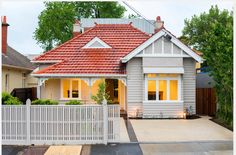 a small house with a red roof and white picket fence in front of the house