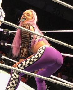 a woman with pink hair is standing in the middle of a wrestling ring wearing purple tights