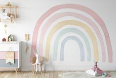 a child's room decorated in pastel colors with a painted rainbow wall mural