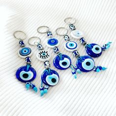 seven evil eye keychains with blue beads and glass eyes are on a white surface