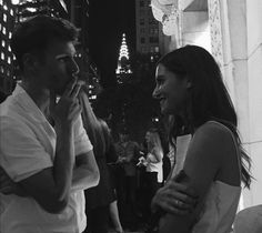 a man and woman standing next to each other in front of tall buildings at night