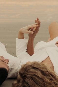 a man and woman laying on the beach next to each other with their hands together