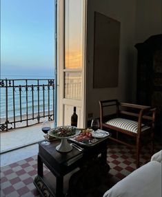 a table with food and wine on it in front of an open door overlooking the ocean