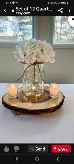 some white flowers are in a glass vase on a wood slice with candles around it