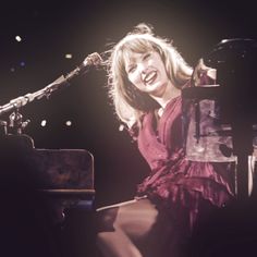 a woman sitting at a piano in front of a microphone