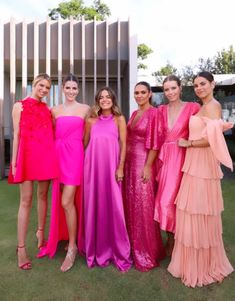 four women in dresses standing next to each other on the grass with their arms around one another