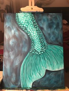 an acrylic painting of a mermaid tail on a easel with paintbrushes