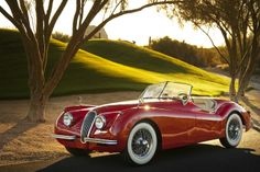 an old red sports car is parked on the side of the road